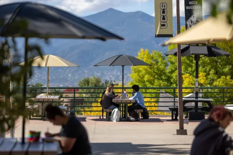 students sitting at a picnic table on campus with mountains in the background